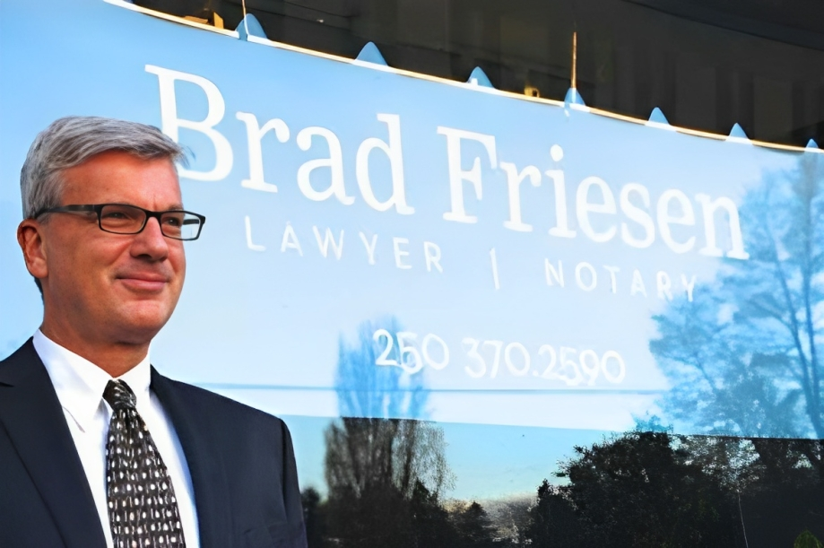 Brad standing in front his office, with a sign saying 'Brad Friesen, Lawyer & Notary' behind him.